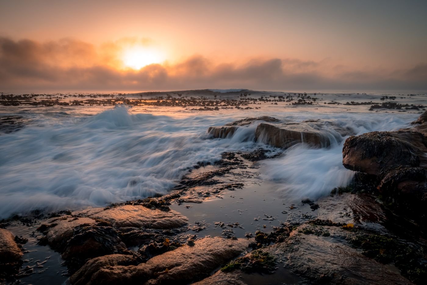 Waves over a rocky Cape Town shoreline at sunset